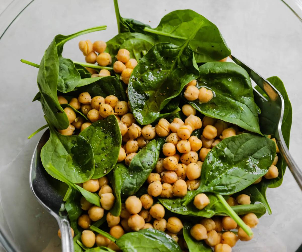 A bowl of a vibrant refreshing salad with golden chickpeas and baby spinach leaves lightly coated in zesty dressing and seasoned with black pepper, made following The Recipe Cloud database.