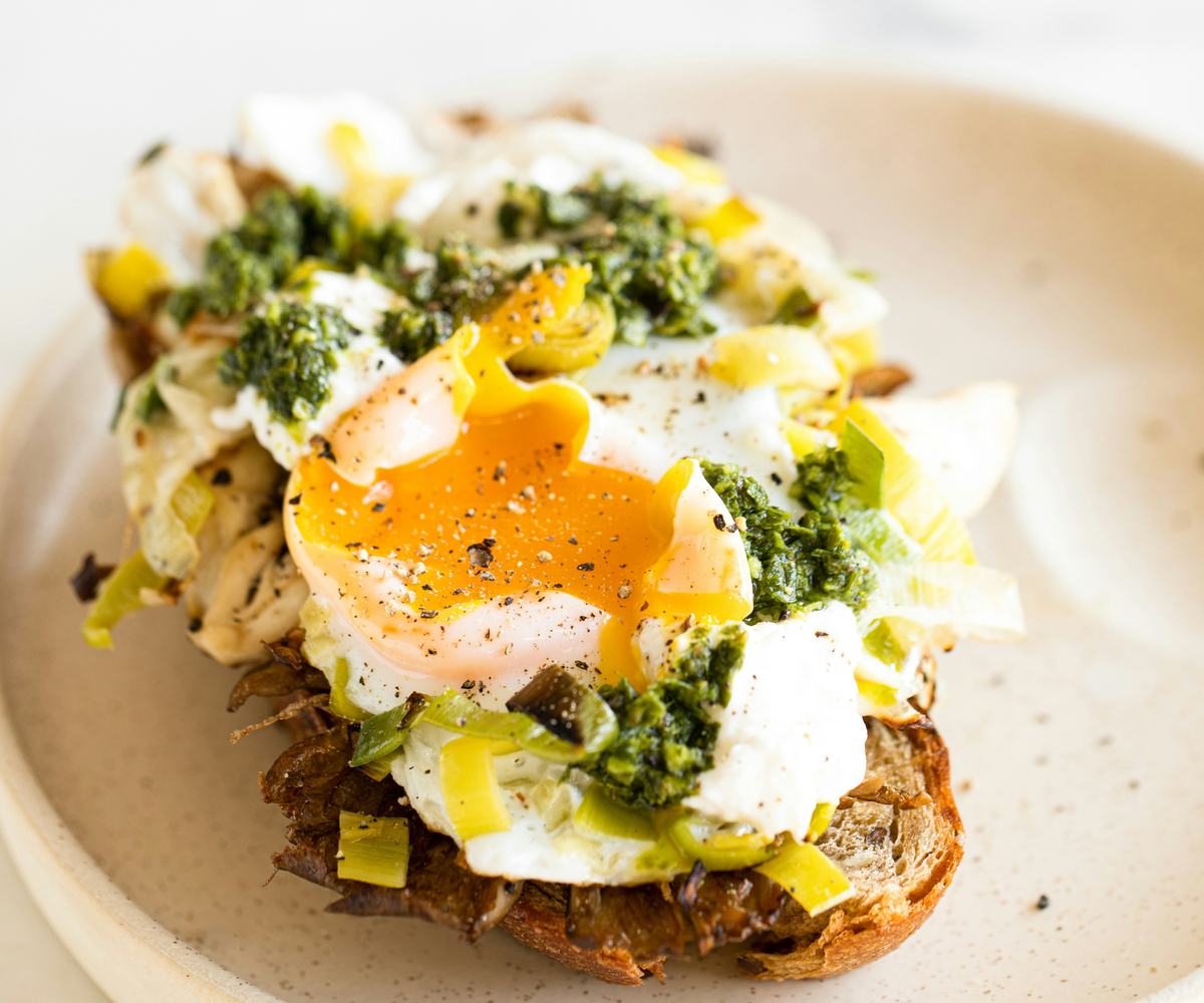 Freshly cooked for 3 minutes poached egg with a soft, runny yolk, served on a toasted slice of bread, finished with fresh green herbs on a plate.