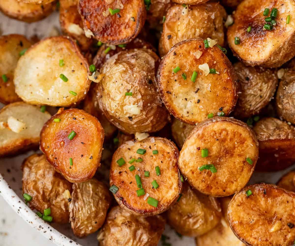 Golden roasted potato halves with garlic notes and caramelized edges. Garnished with fresh chopped herbs and served right from the oven to enjoy its crispiness.