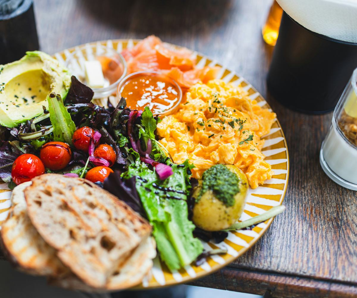 A gourmet breakfast plate featuring soft and fluffy scrambled eggs,. Served with smoked salmon, fresh avocado, cherry tomatoes, and crusty bread for a perfectly balanced meal.