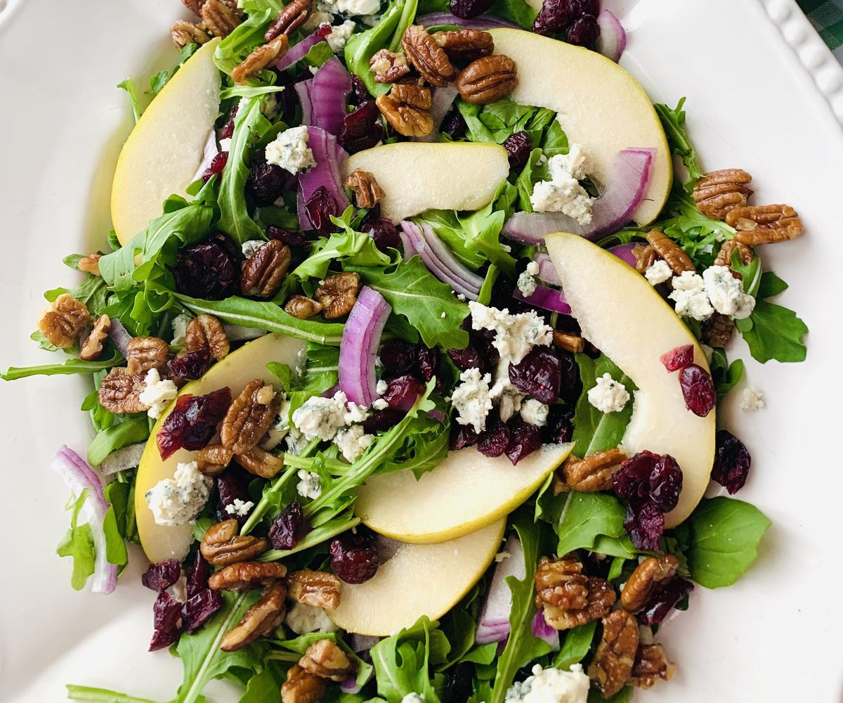 A fresh arugula salad with pear slices, crunchy toasted pecans, tangy blue cheese, and a touch of red onion — a vibrant mix of textures and flavors perfect for any occasion.