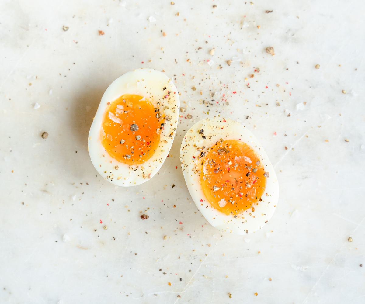 A halves of freshly soft-boiled egg with jammy yolk, sprinkled with salt and pepper on a light surface.
