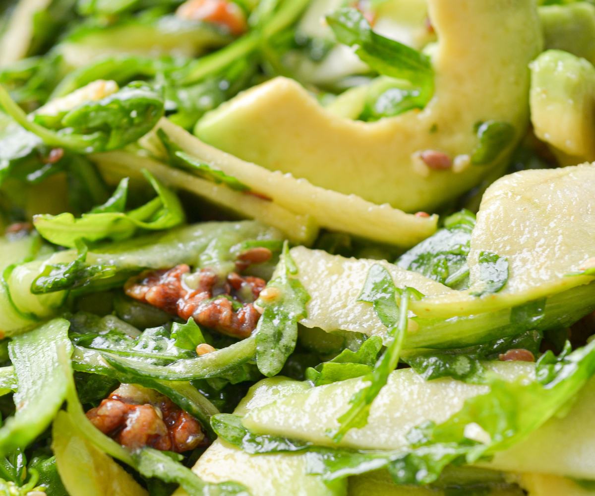 Fresh arugula salad with avocado slices, thin ribbons of cucumber, apple, and toasted walnuts, lightly coated in a glossy dressing made following by The Recipe Cloud.