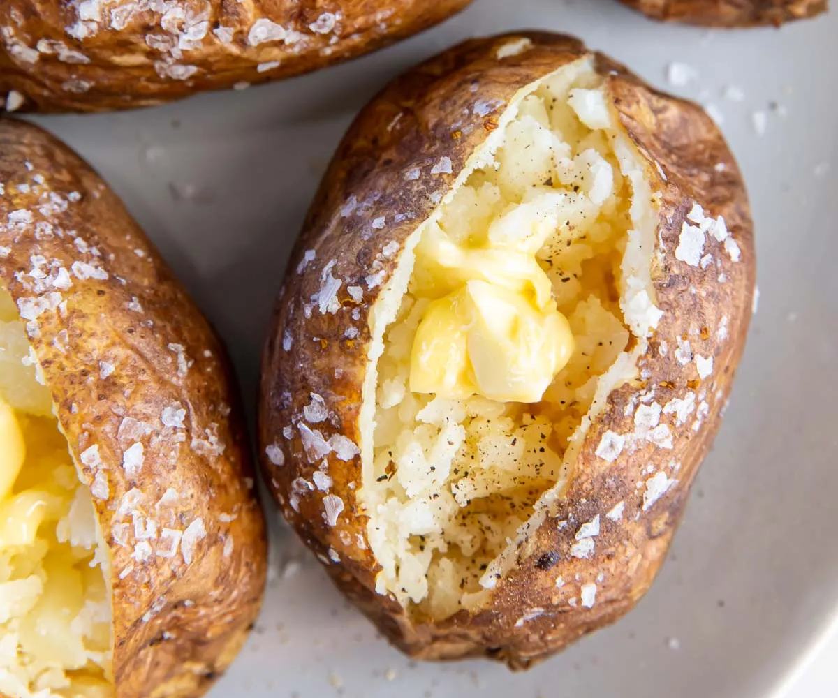 Four whole potatoes, perfectly baked until the skin forms a crunchy salty-peppery layer, cross-cut to reveal its soft and fluffy texture, served with a generous amount of butter.