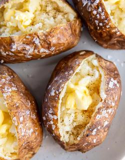Four whole potatoes, perfectly baked until the skin forms a crunchy salty-peppery layer, cross-cut to reveal its soft and fluffy texture, served with a generous amount of butter.